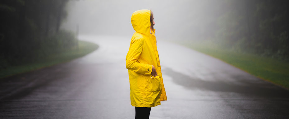 Girl in yellow coat standing on the middle on the road under rain