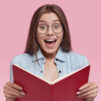 photo-intelligent-european-female-wonk-holds-opened-book-feels-happy-read-romantic-story-end-feels-excited-with-unexcpected-event-wears-jean-jacket-round-eyeglasses-stands-indoor