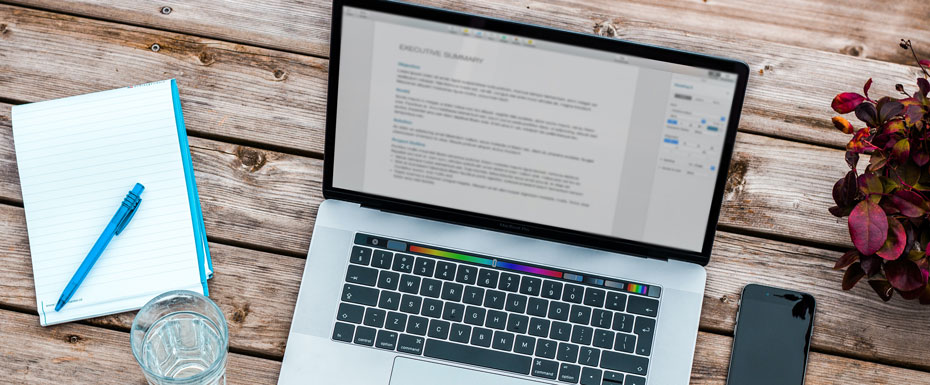 Laptop with text on it with blue/white notebook close to it and pen on notebook. Burgundy flower on the right with phone laying on the wooden table outside