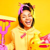 joyful dark skinned housemaid smiles broadly wears sweatshirt protective rubber gloves holds laundry basket mop happy finish housework isolated yellow