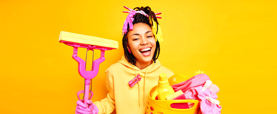 joyful dark skinned housemaid smiles broadly wears sweatshirt protective rubber gloves holds laundry basket mop happy finish housework isolated yellow