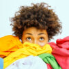 young afro-american woman surrounded by different colorful clothes sorts out wardrobe focused isolated white wall blank space your advertising content nothing wear concept