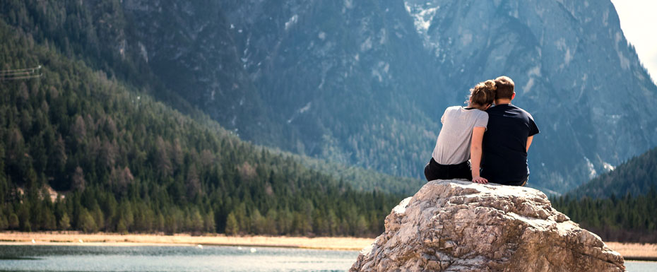 A couple sits on a rock looking out over a lake