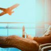 man sitting on gang chair with feet on luggage looking at airplane