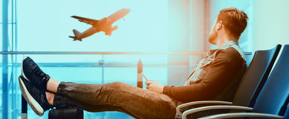 man sitting on gang chair with feet on luggage looking at airplane