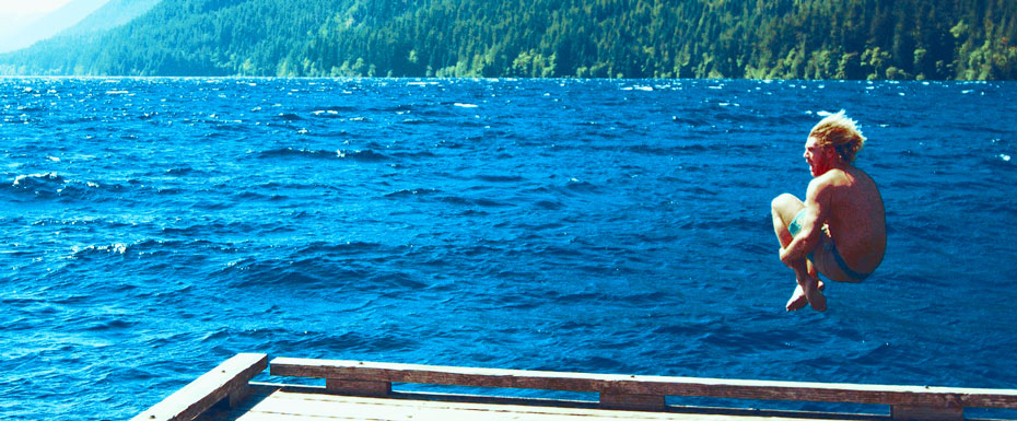 Topless Person Jumping Towards Water From White Wooden Dock