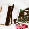 gold colored framed sunglasses on brown hat beside white and black leather wristlet surrounded-by-photos-on-white and gray floral textile